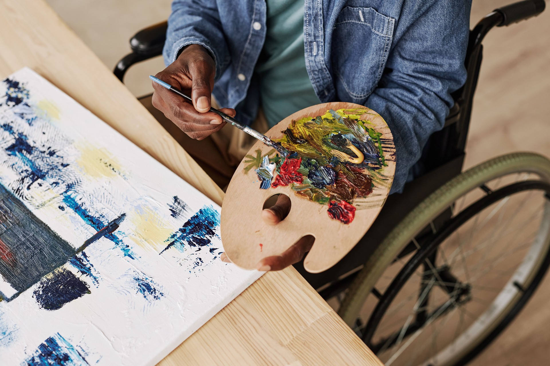 Above view of young black man with disability mixing paints